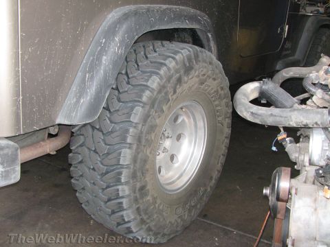 1987 Suzuki Samurai - A Jeep Wrangler is shown from the side, large off-road tires and visible engine parts, suggesting it is in a workshop or undergoing mainten…