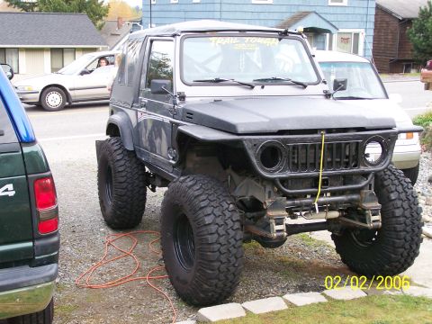 1988 Suzuki Samurai - This heavily modified off-road vehicle is parked next to another car, with a building in the background.