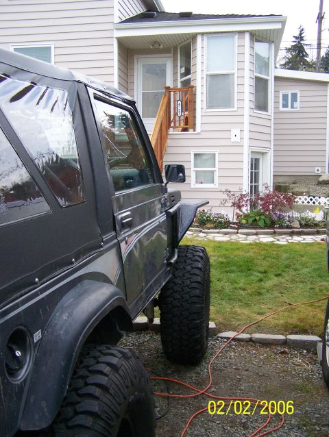 1988 Suzuki Samurai - A dark gray 1988 Suzuki Samurai with oversized tires is parked next to a house.