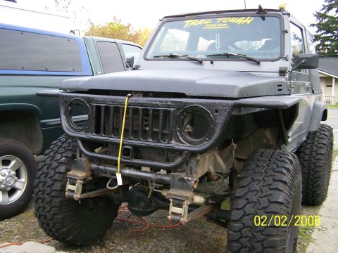 1988 Suzuki Samurai - A gray 1988 Suzuki Samurai is parked next to a pickup truck, showing its modified front end and large tires.