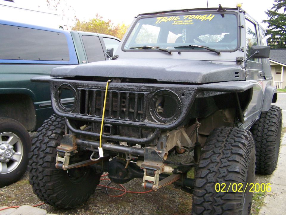 Modified black Suzuki SUV, front clip stripped, big mud tires, Trail Tough windshield banner
