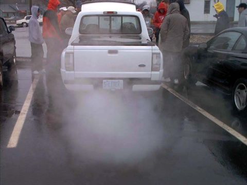 2000 Ford Crown Victoria - Rear view of a white Ford Ranger extended-cab pickup doing a burnout in a wet parking lot, tire smoke billowing across the frame and a vani…