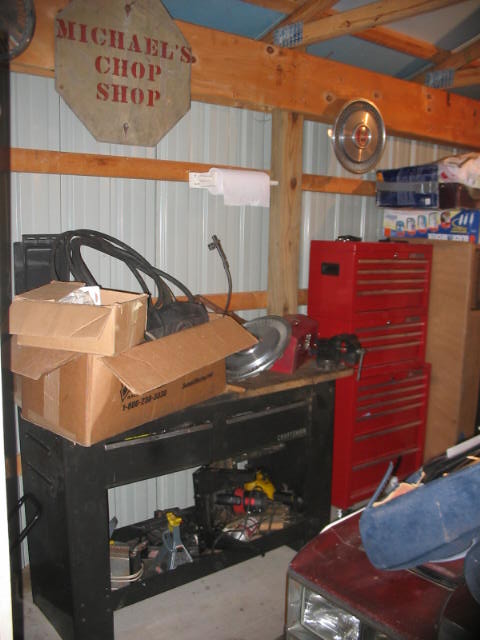1900 Ford Wagon - A cluttered workshop scene displays tool chests, cardboard boxes, and the hood of a red vehicle.