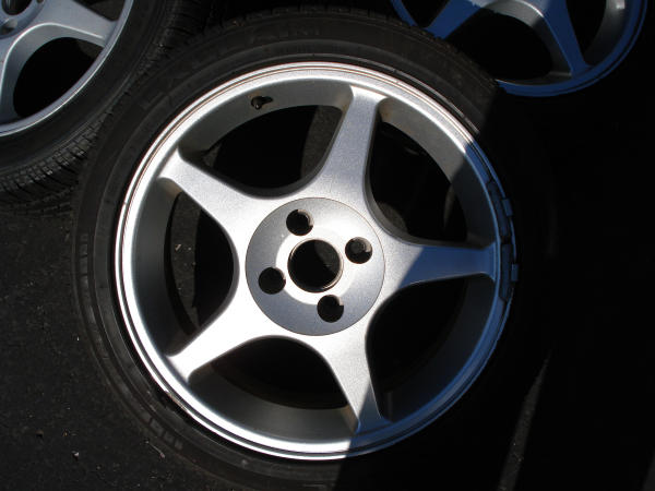 Close-up of two silver 5-spoke alloy wheels with tires. One wheel is in focus