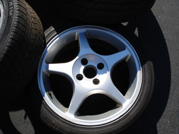 Silver five-spoke alloy wheel with tire, next to other tires
