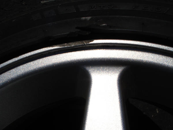 Close-up of a tire sidewall and a silver alloy wheel with visible damage on the tire