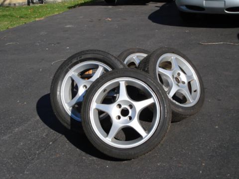 1979 Ford Bronco - Four aftermarket alloy wheels with tires are displayed on a paved surface, with a portion of a car visible in the background.