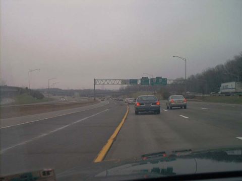 2000 Ford Crown Victoria - Two cars travel down a multi-lane highway on a cloudy day, with a truck visible in the distance.