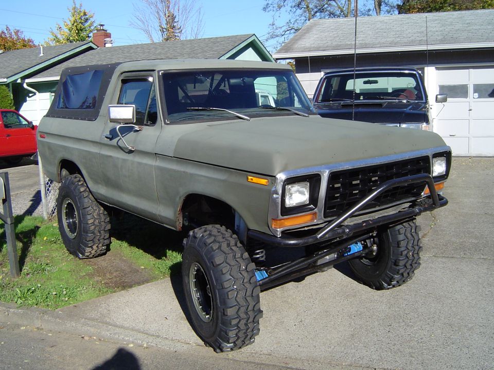 Olive green 1978 Ford Bronco with off-road tires and brush guard, parked in driveway