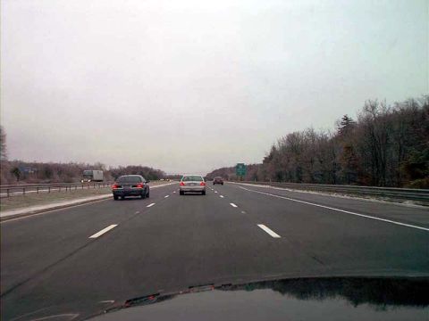 2000 Ford Crown Victoria - Driving on a highway with several cars ahead and trees lining the right side.