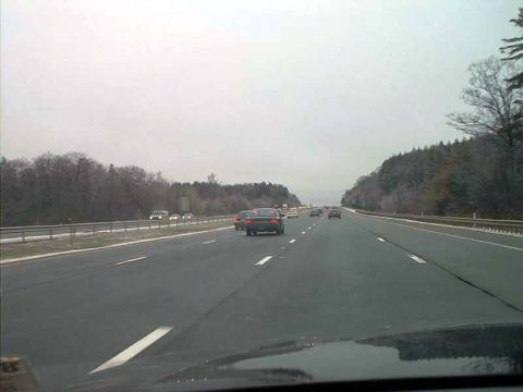 2000 Ford Crown Victoria - Traffic moves along a multi-lane highway on a cloudy day, with trees visible on the embankment.