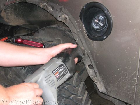 1987 Suzuki Samurai - A person is modifying the fender of a vehicle with a reciprocating saw, revealing a large off-road tire.