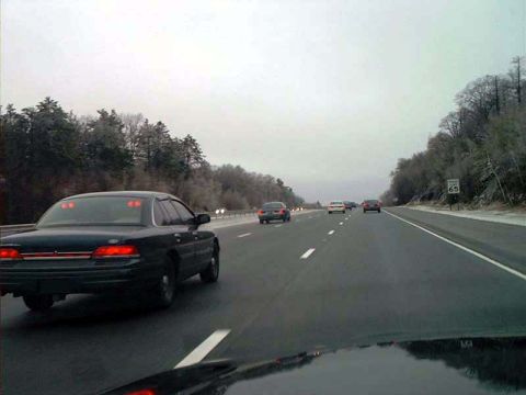 2000 Ford Crown Victoria - A black 2000 Ford Crown Victoria is seen from behind on a highway with other vehicles.