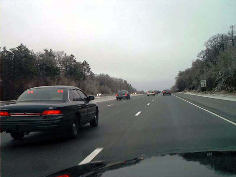 Black 2000 Ford Crown Victoria sedan driving on a highway, rear view
