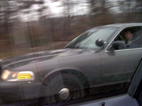 2000 Ford Crown Victoria - Motion-blurred rolling shot taken through a car window of a dark Ford Crown Victoria sedan driving alongside on a rural road, with its ambe…
