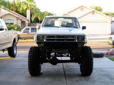 1986 Toyota Hilux - This modified Toyota pickup truck features oversized tires and a lifted suspension, with another vehicle visible to the side.