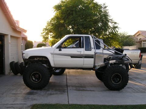 1986 Toyota Hilux - A heavily modified white pickup truck with large off-road tires and a custom roll cage is parked in a suburban driveway.