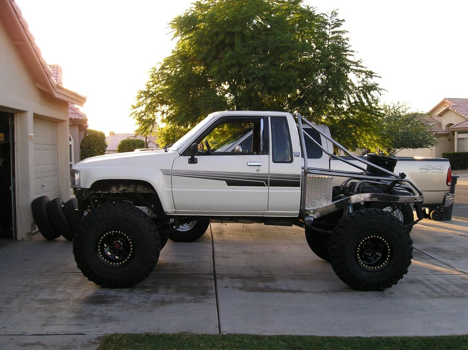 White pickup truck with oversized tires and roll cage, parked in a driveway