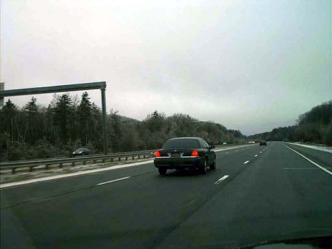 2000 Ford Crown Victoria - A black 2000 Ford Crown Victoria is seen driving on a highway under an overcast sky.