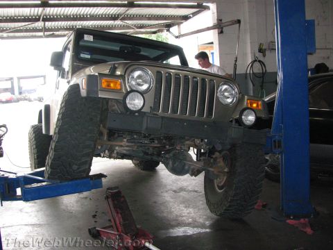1987 Suzuki Samurai - A Jeep Wrangler is being serviced in a garage, elevated on a hydraulic lift.