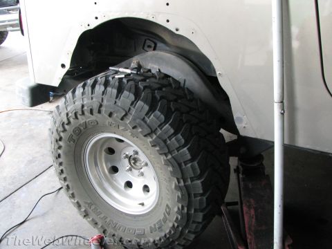 1987 Suzuki Samurai - Close-up of a vehicle's rear wheel well and tire, showing modifications and a jack.