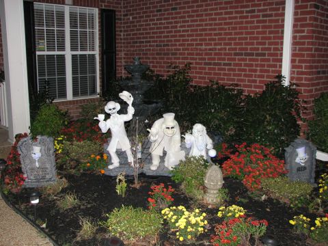 1991 Ford Bronco - Halloween decorations with ghost figures and tombstones are displayed in a garden bed.