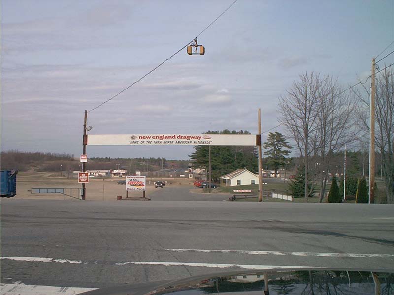 New England Dragway entrance sign spanning the drive over an empty asphalt lot