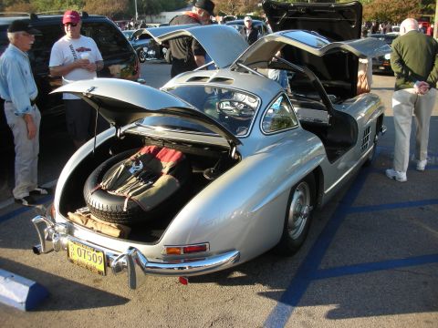 1998 Ford Crown Victoria - Silver classic gullwing-door coupe with its trunk and door open at a daytime car show, spare tire and luggage visible.