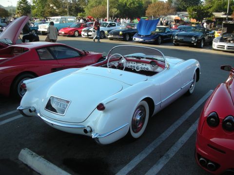 1998 Ford Crown Victoria - White early Chevrolet Corvette roadster shown rear three-quarter in a lot lined with classic and red sports cars.