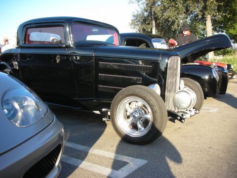1998 Ford Crown Victoria - Black chopped hot rod coupe shown in profile on chrome wheels among other cars in a sunlit lot.