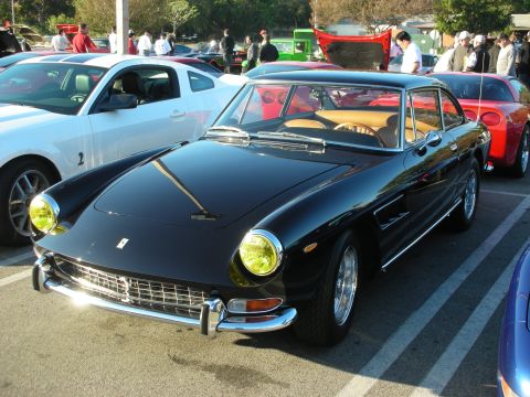 1998 Ford Crown Victoria - Black vintage Ferrari 2+2 coupe with yellow headlights, parked front three-quarter at a busy morning car show.