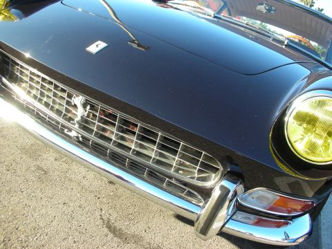 1998 Ford Crown Victoria - Low close-up of a black Ferrari front showing its chrome eggcrate grille, prancing-horse badge and yellow headlight.