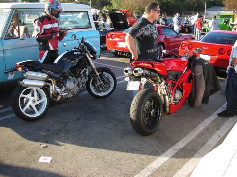 1998 Ford Crown Victoria - black Ducati naked motorcycle and a red Ducati sportbike parked in a lot as onlookers gather.
