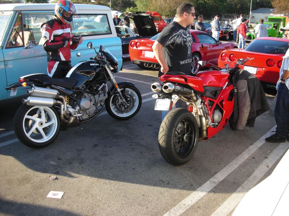 Black Ducati naked bike and red Ducati sportbike parked at an outdoor car meet