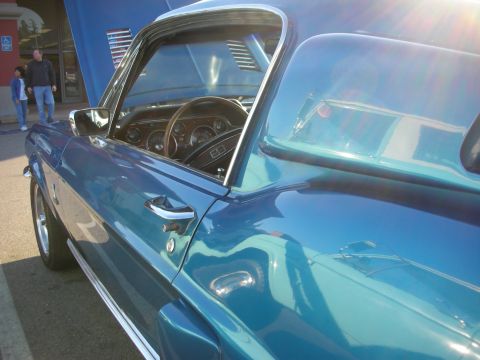 1998 Ford Crown Victoria - Sunlit profile of a teal classic Mustang fastback, looking through the side window to its wood-rim dash.
