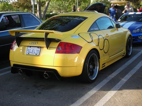 1998 Ford Crown Victoria - Yellow Audi TT coupe shown rear three-quarter with a rear wing, black wheels and sponsor decals at a car meet.