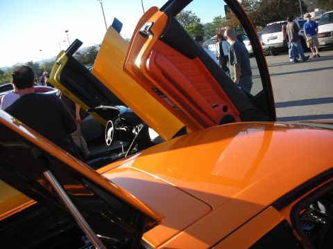 1998 Ford Crown Victoria - Orange Lamborghini with scissor doors raised, revealing a red-and-black leather interior at an outdoor car show.