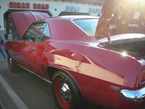 1998 Ford Crown Victoria - red Chevrolet Camaro coupe shown in profile with its hood raised, parked at the curb in front of a Cigar Road deli and restaurant.