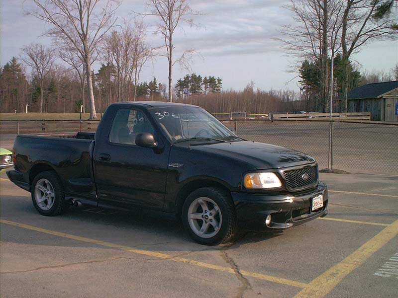 Black 1999 Ford F-150 Lightning pickup truck, front 3/4 view, parked on asphalt with yellow lines