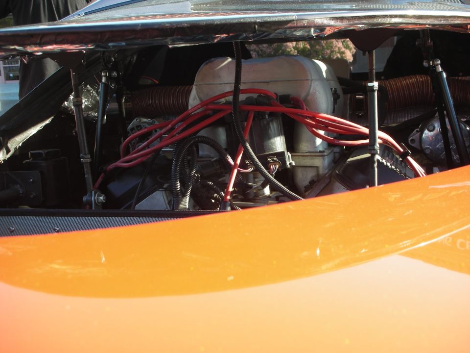 Engine bay of an orange car showing a V8 with red spark-plug wires