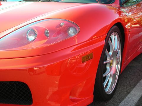 1998 Ford Crown Victoria - Close-up of a red Ferrari 360's front fender showing the prancing-horse shield, headlight, and silver multi-spoke wheel.