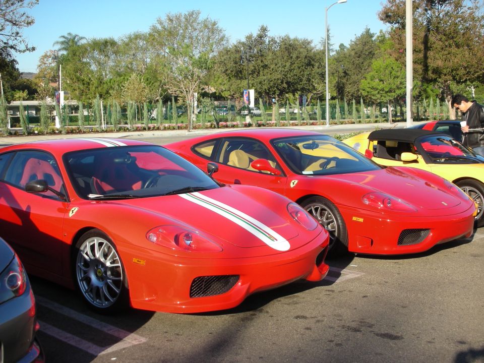 Two red Ferrari 360 coupes parked side by side, one with a racing stripe