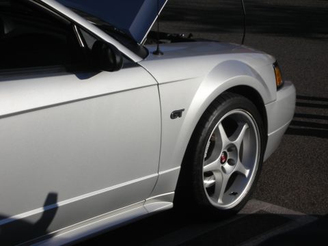 1998 Ford Crown Victoria - Front fender of a silver New Edge Ford Mustang showing the GT badge and a silver five-spoke wheel.