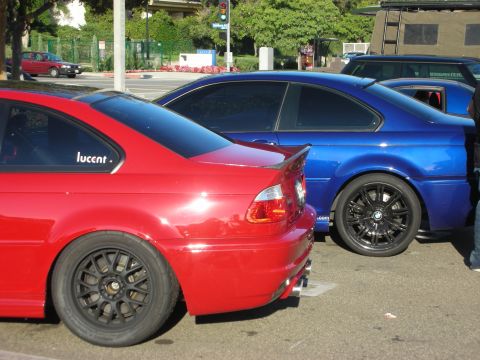 1998 Ford Crown Victoria - red coupe and a blue coupe sit parked side by side on black wheels, viewed from the rear three-quarter at a sunny lot.