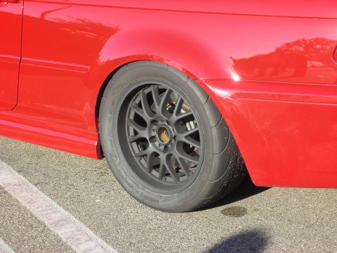 1998 Ford Crown Victoria - Close-up of a red car's rear quarter showing a gray multi-spoke wheel wrapped in a smooth track tire on pavement.