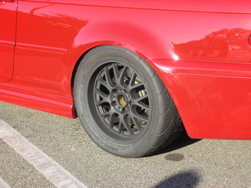 Close-up of a red car's rear wheel with gray multi-spoke wheel and track tire