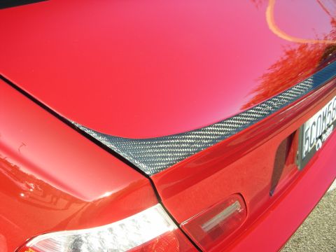1998 Ford Crown Victoria - glossy carbon-fiber spoiler lip runs across the trunk of a red car, with the taillight and a license plate just in frame.