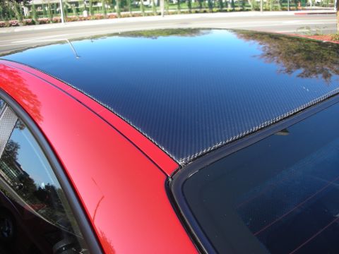 1998 Ford Crown Victoria - exposed carbon-weave roof of a red coupe gleams in sunlight above the rear window glass.