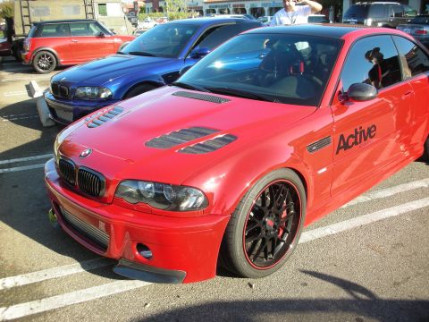 1998 Ford Crown Victoria - red BMW coupe with a vented hood, black multi-spoke wheels and 'Active' lettering sits in a lot beside a blue car and a Mini.