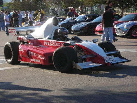 1998 Ford Crown Victoria - red-and-white open-wheel single-seat race car with a helmeted driver and 'STREET LEGAL' lettering rolls through a meet.